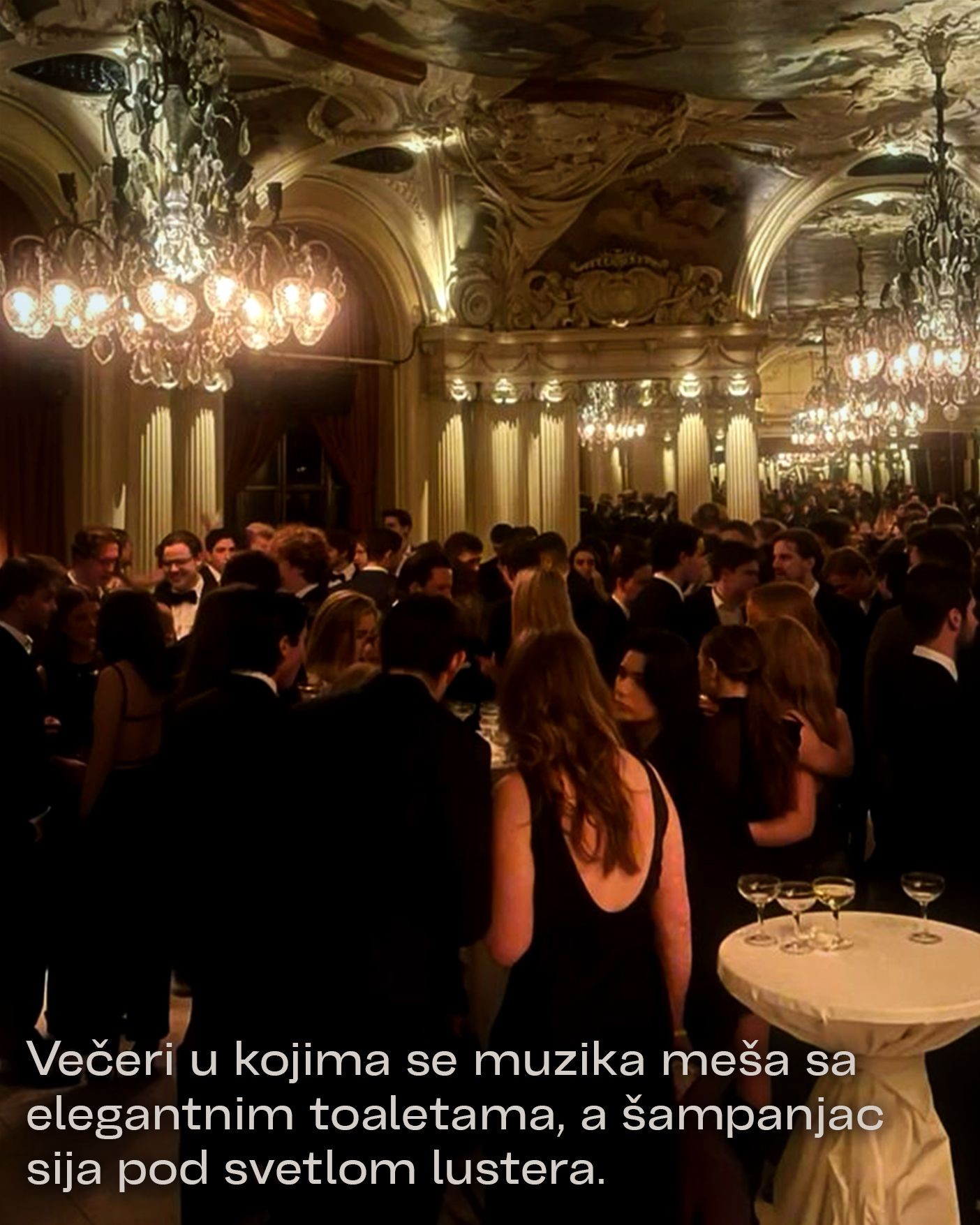 Elegant ballroom event with guests in formal attire, chandeliers, and tables with champagne glasses.