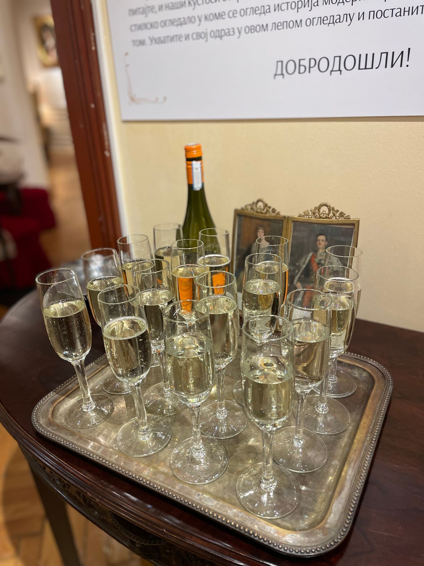 Tray of filled champagne glasses on a wooden table beside an open wine bottle and decorative photo frames.