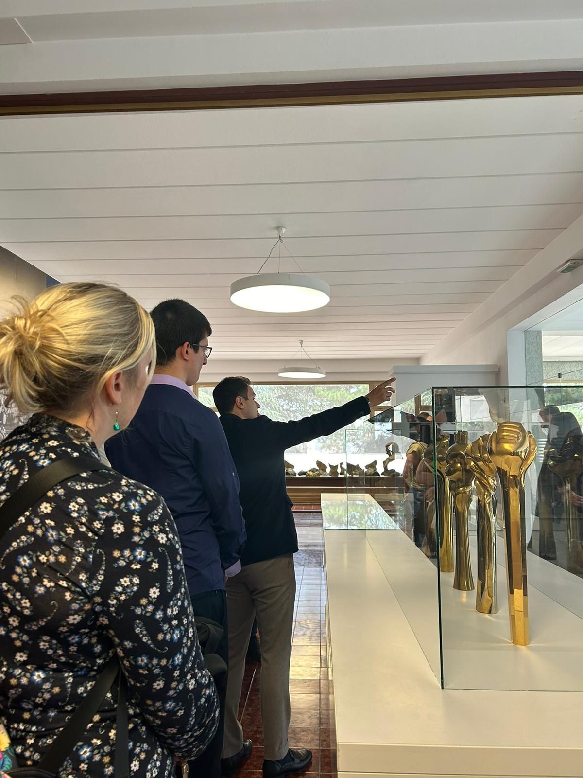 Group of people viewing illuminated golden sculptures in a glass display case within a modern gallery setting.