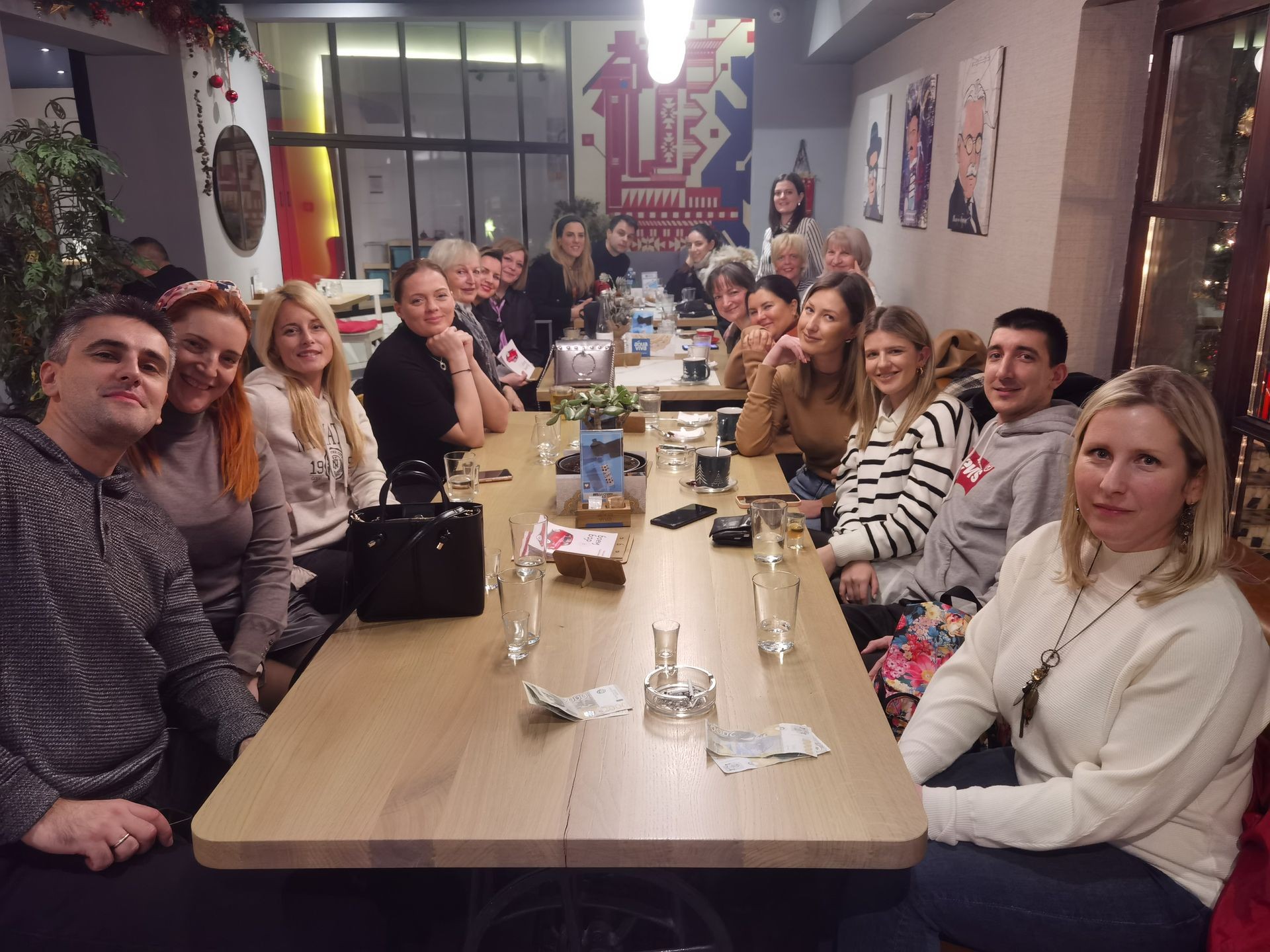 Group of people sitting together at a long table in a restaurant, smiling towards the camera.