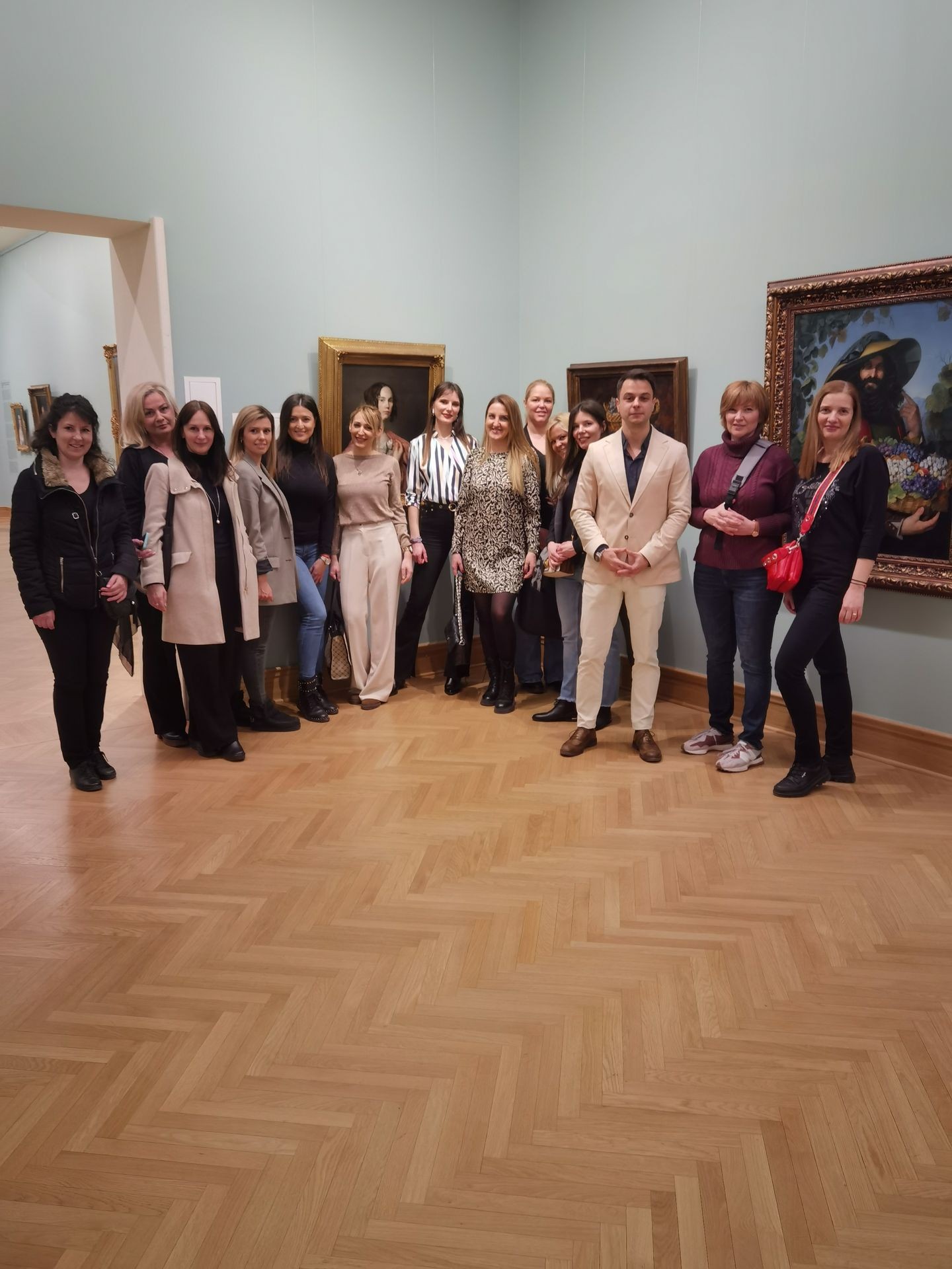 Group of people standing in an art gallery with paintings on the wall and wooden flooring.