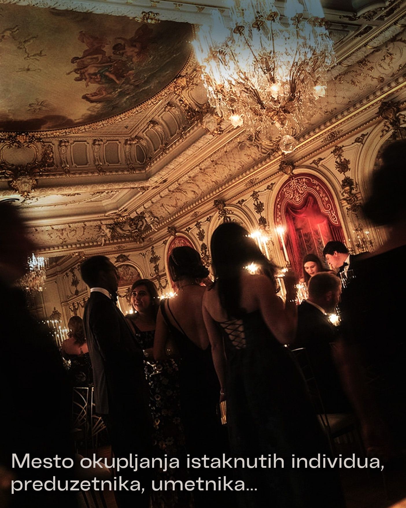Elegant ballroom with chandelier and people in formal attire socializing under ornate ceiling.