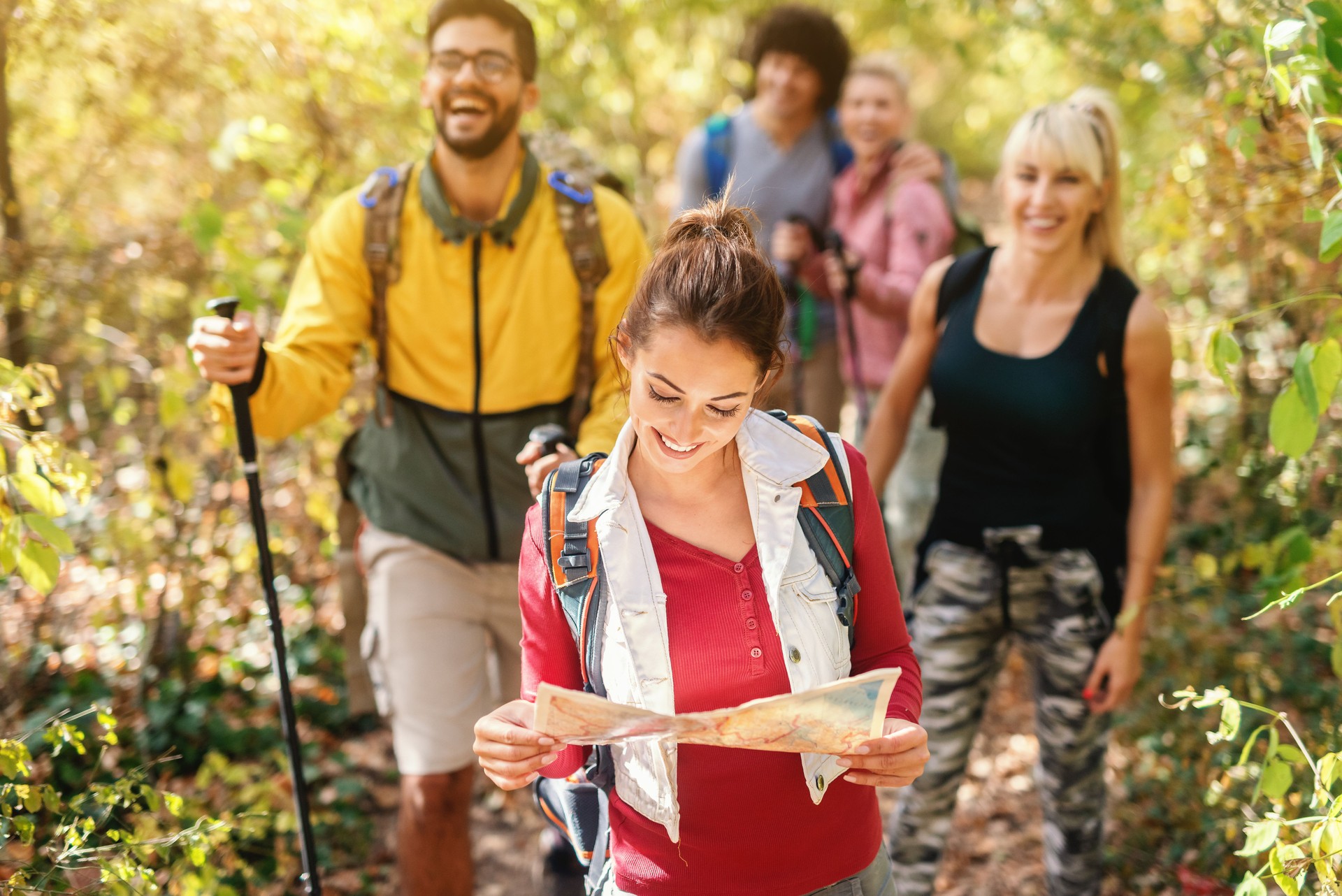 Smiling beautiful brunette holding map and leading the rest of hikers through woods in autumn.